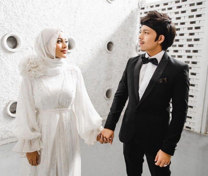 2. Nampak anggun dengan balutan gaun putih dan hijab, Aurel menggandeng tangan sang suami dengan mesra.